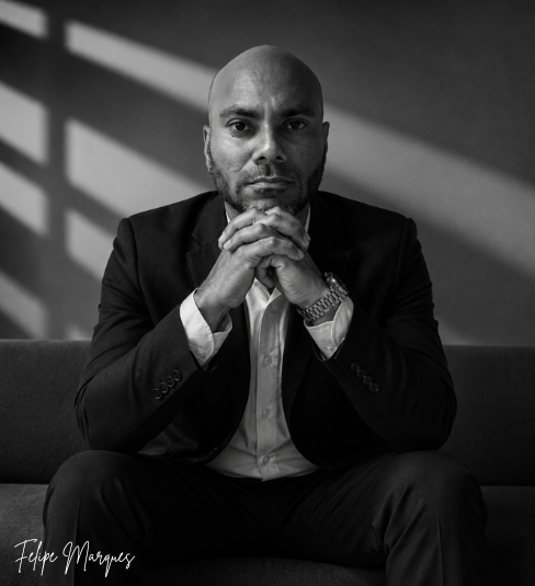Retrato em preto e branco de executivo sentado, olhando para a câmera com expressão séria, em ambiente corporativo minimalista.